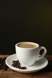 Photo of Cup of hot aromatic coffee and roasted beans on wooden table against dark background