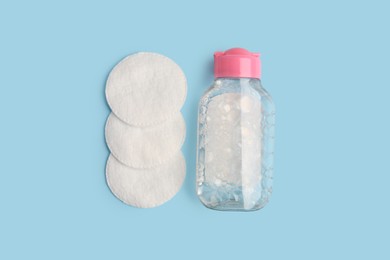 Photo of Bottle of makeup remover and cotton pads on light blue background, flat lay