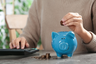 Woman putting money into piggy bank at table, closeup