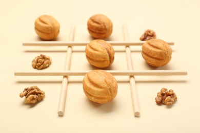 Photo of Tic tac toe game made with walnuts and cookies on beige background, closeup