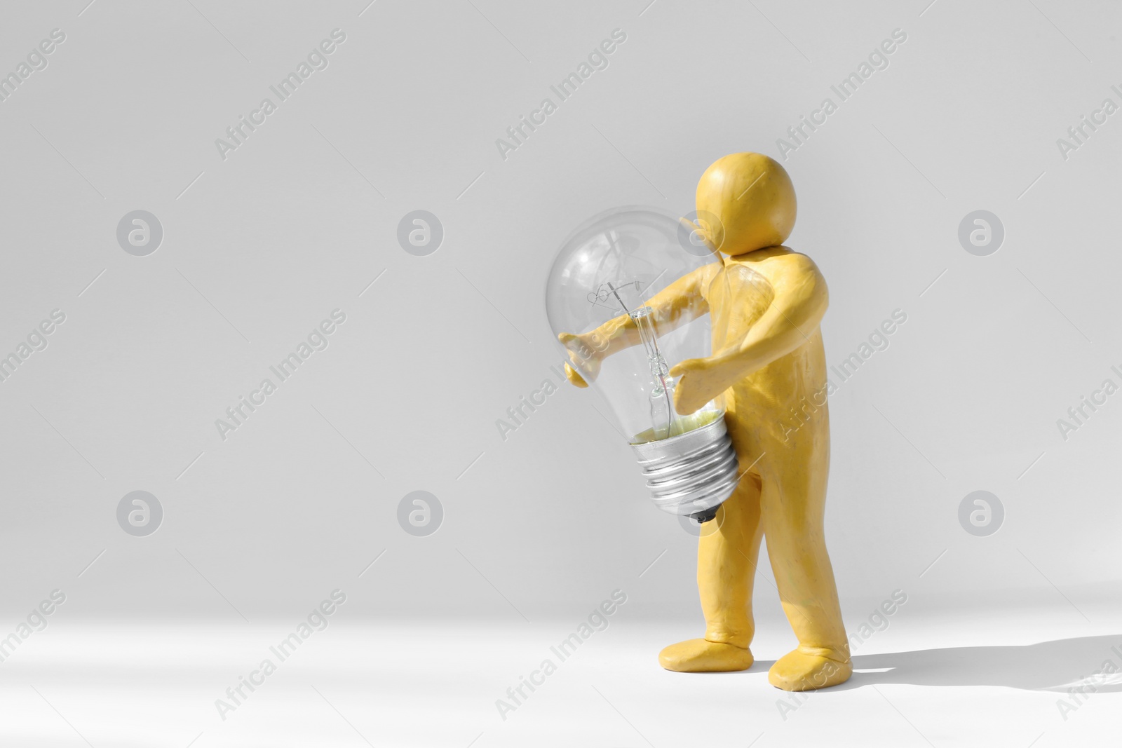 Photo of Human figure made of plasticine holding light bulb on white background. Space for text