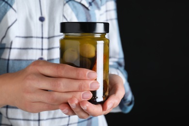 Photo of Woman holding jar with pickled olives against black background, closeup