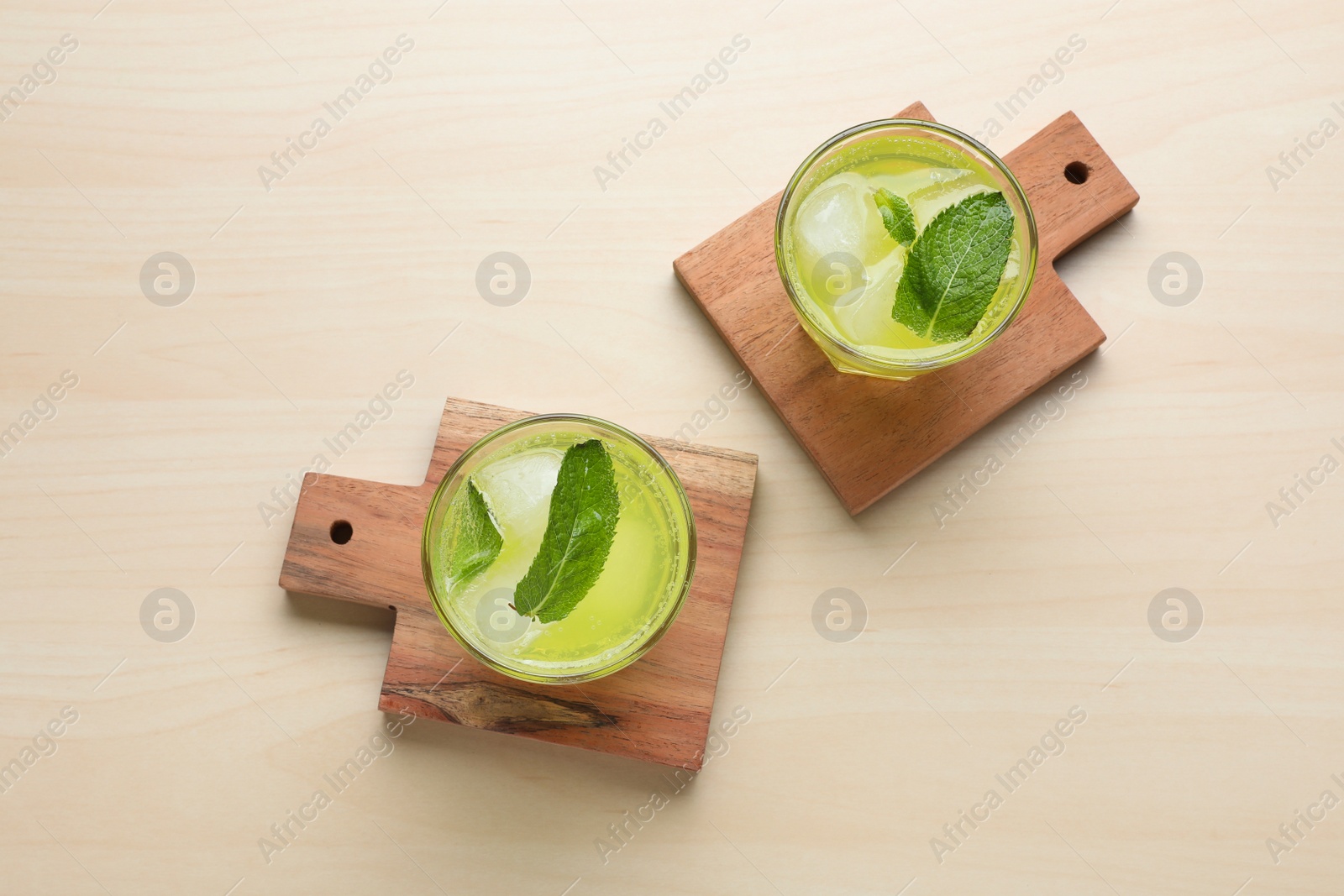 Photo of Glasses of lemonade and stylish wooden cup coasters on table, flat lay