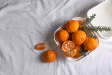 Photo of Box with delicious ripe tangerines and fir branches on white bedsheet, flat lay. Space for text
