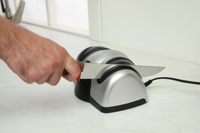 Photo of Man sharpening knife with electrical tool at white table, closeup