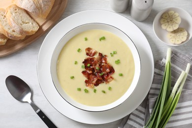 Photo of Tasty potato soup with bacon in bowl served on white wooden table, flat lay