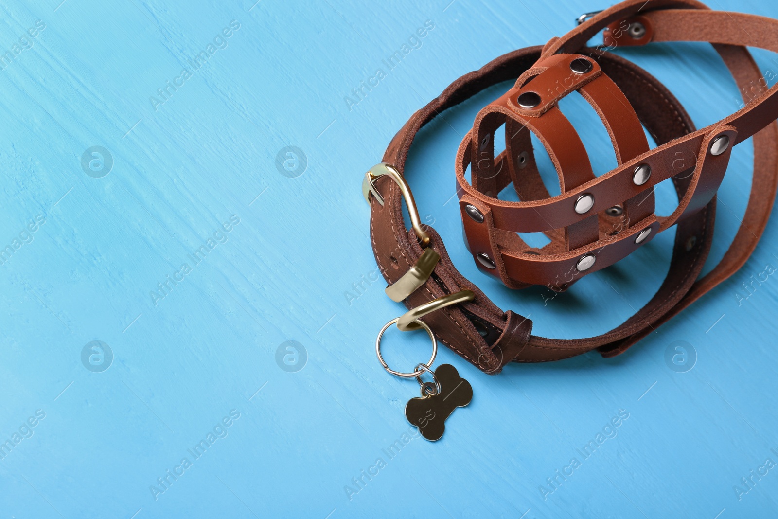 Photo of Brown leather dog muzzle and collar on light blue wooden table. Space for text