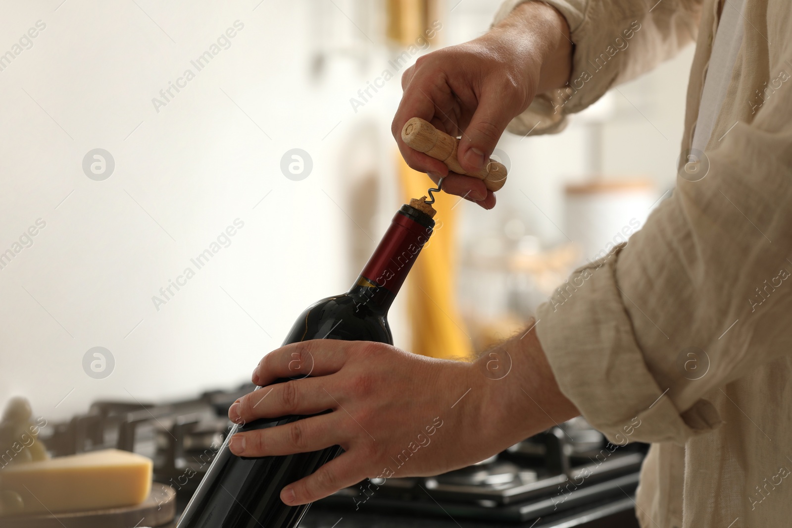 Photo of Man opening wine bottle with corkscrew indoors, closeup. Space for text