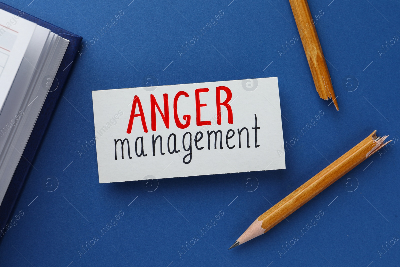 Photo of Card with words Anger Management, notebook and broken pencil on blue background, flat lay