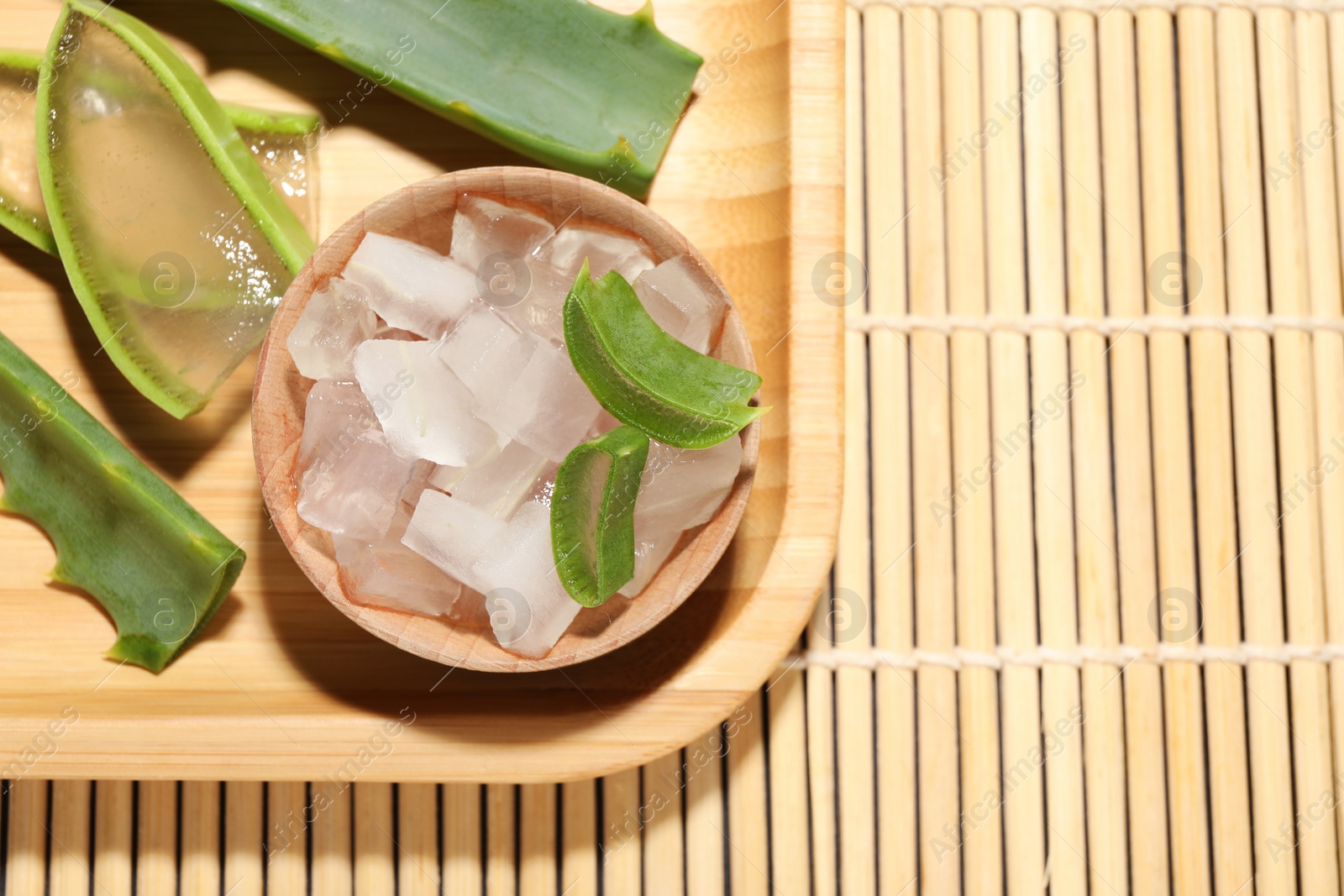 Photo of Aloe vera gel and slices of plant on bamboo mat, top view. Space for text