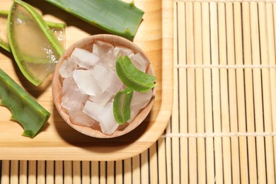 Photo of Aloe vera gel and slices of plant on bamboo mat, top view. Space for text