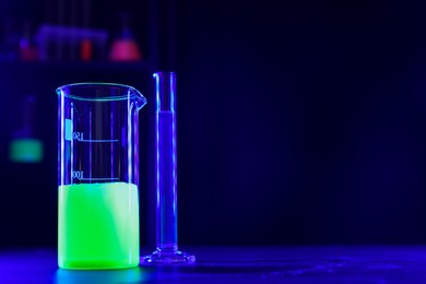 Laboratory glassware with luminous liquids on table, space for text