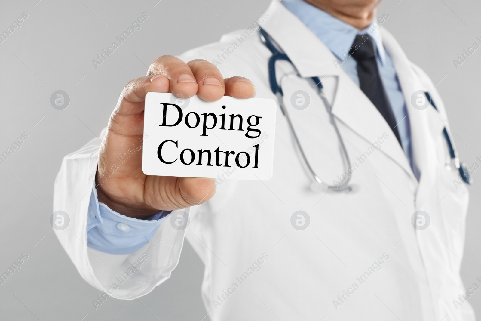 Image of Doctor holding card with text Doping Control on light grey background, closeup