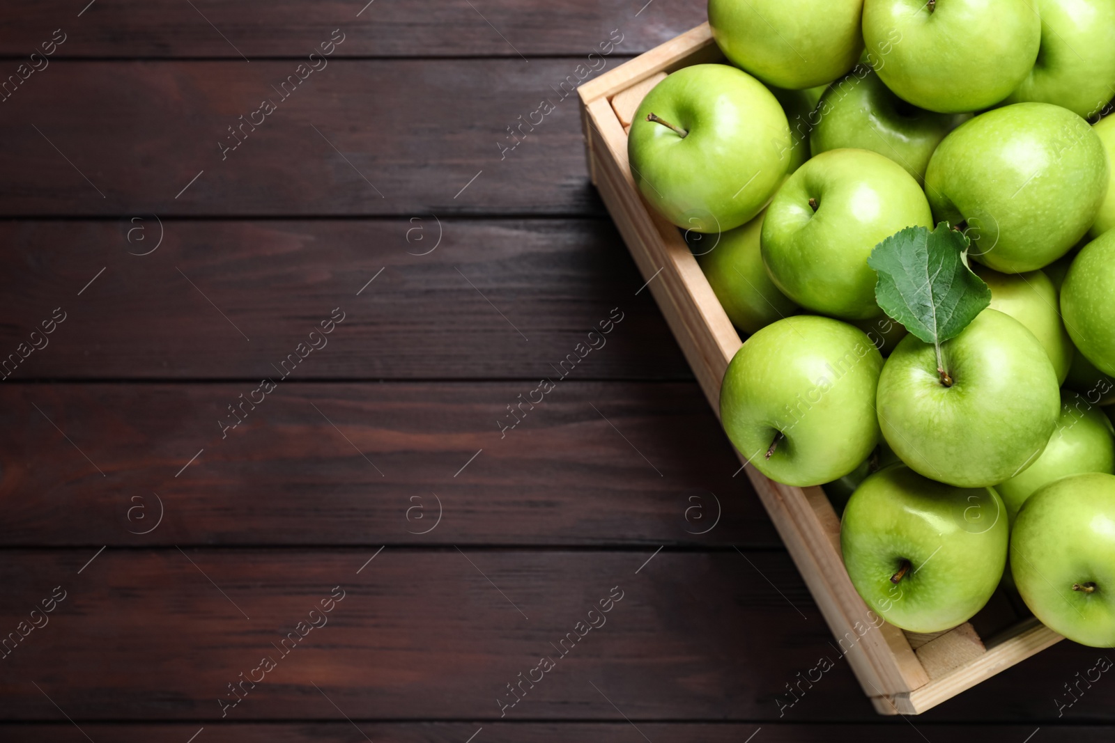 Photo of Juicy green apples in crate on wooden table, top view. Space for text