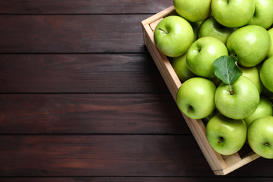 Juicy green apples in crate on wooden table, top view. Space for text