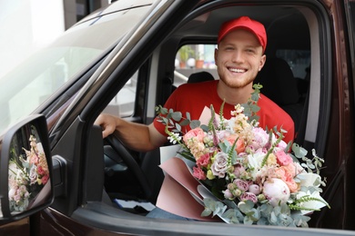 Photo of Delivery man with beautiful flower bouquet sitting in car