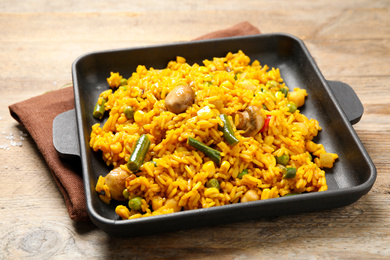 Photo of Delicious rice pilaf with vegetables on wooden table