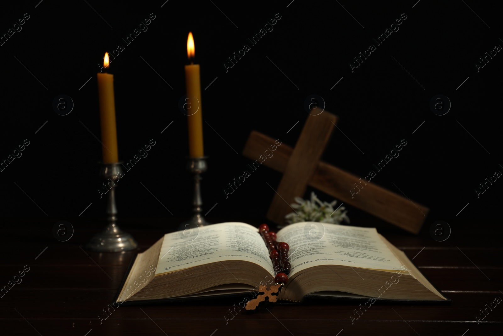 Photo of Crosses, rosary beads, Bible and church candles on wooden table