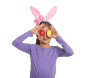 Photo of Little girl in bunny ears headband holding Easter eggs near eyes on white background