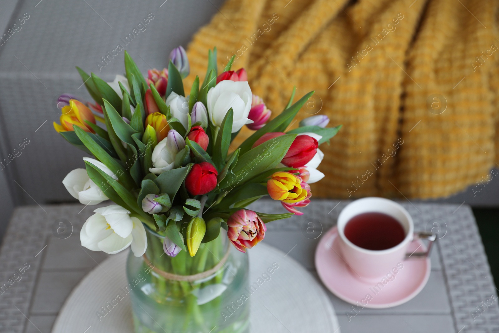 Photo of Beautiful bouquet of colorful tulips and cup with drink on rattan garden table