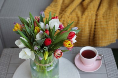 Photo of Beautiful bouquet of colorful tulips and cup with drink on rattan garden table