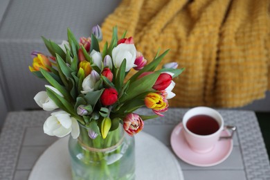 Beautiful bouquet of colorful tulips and cup with drink on rattan garden table