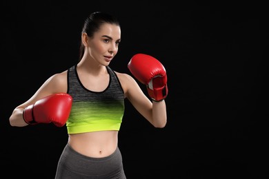 Photo of Beautiful woman in boxing gloves training on black background. Space for text