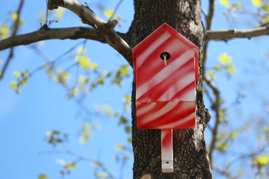 Photo of Red and white bird house on tree outdoors. Space for text