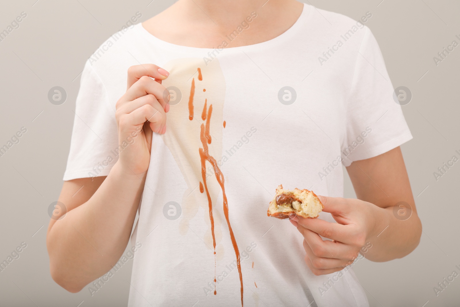 Photo of Woman holding pastry and showing stain from condensed milk on her shirt against light grey background, closeup