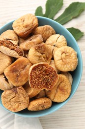 Bowl with tasty dried figs and green leaf on white wooden table, top view