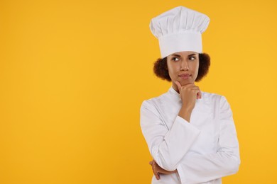 Photo of Thoughtful female chef in uniform on orange background. Space for text