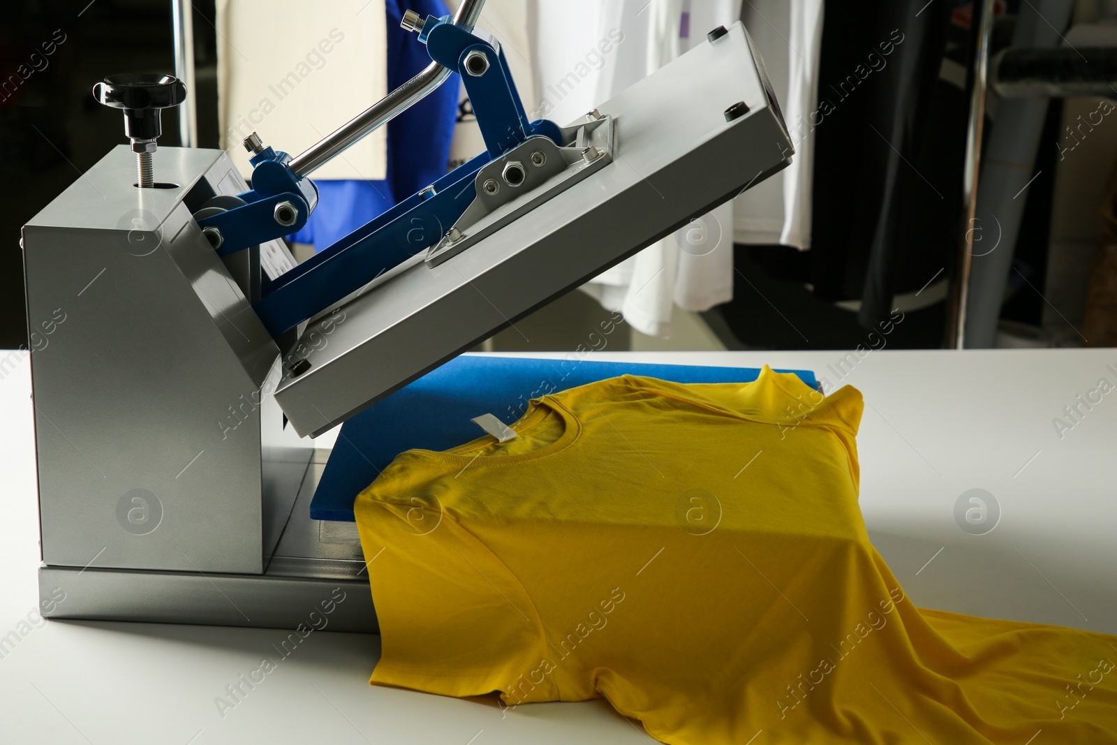 Photo of Printing logo. Heat press with yellow t-shirt on white table