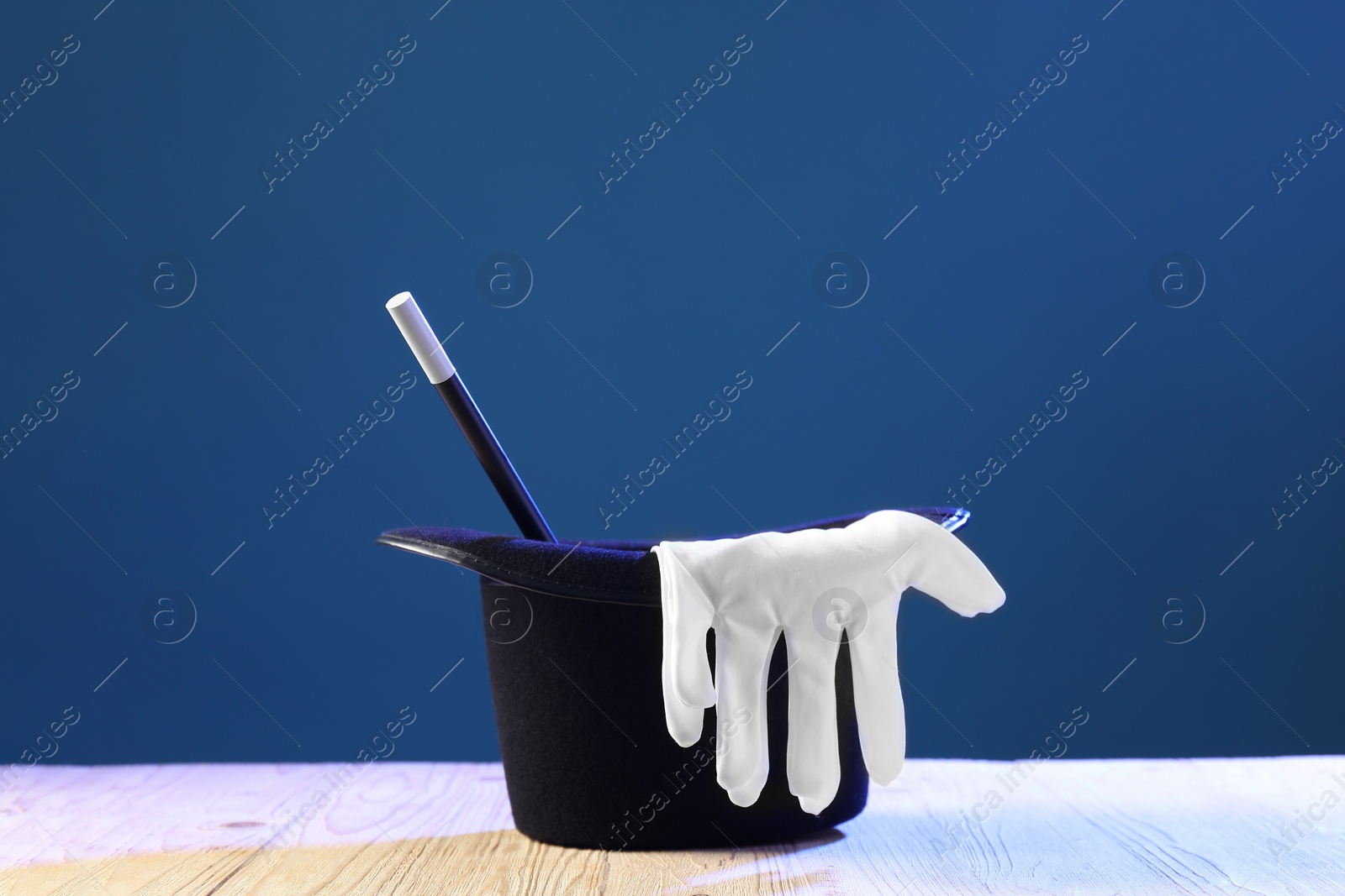 Photo of Magician's hat, wand and gloves on wooden table against blue background