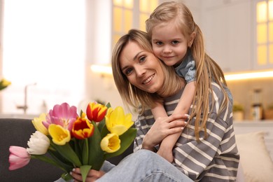 Photo of Little daughter congratulating her mom with Mother`s Day at home. Woman holding bouquet of beautiful tulips