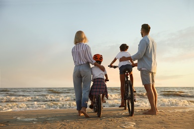 Photo of Family with bicycles on sandy beach near sea, back view