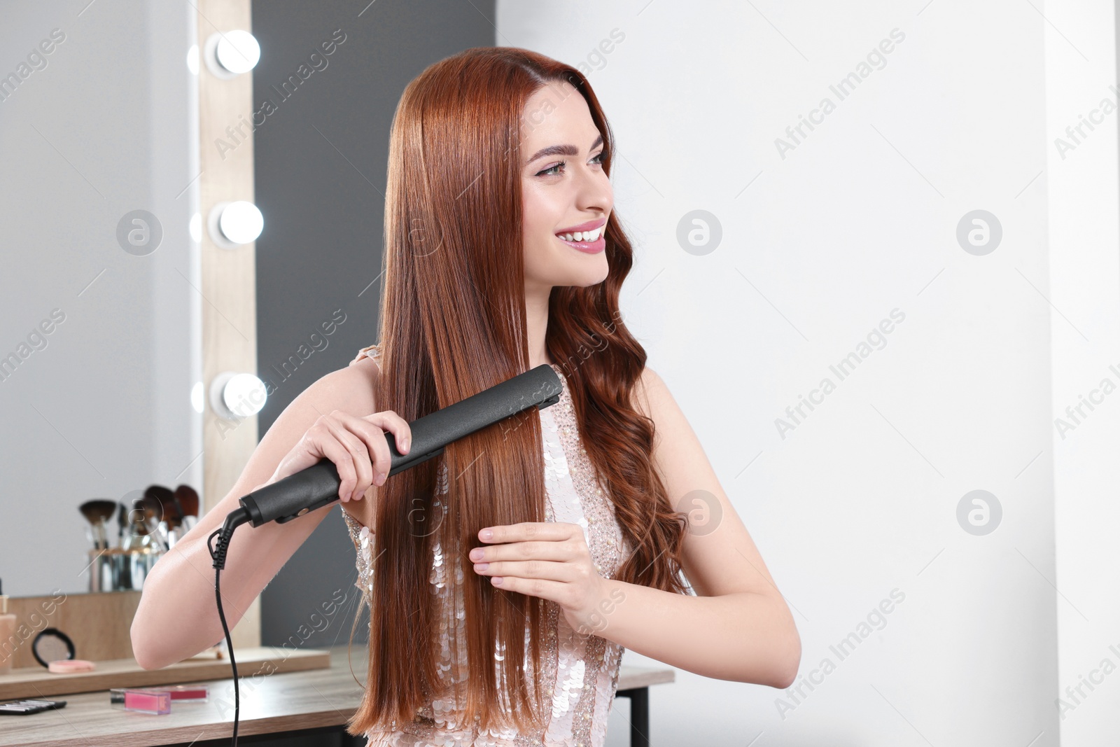 Photo of Beautiful woman using hair iron in room