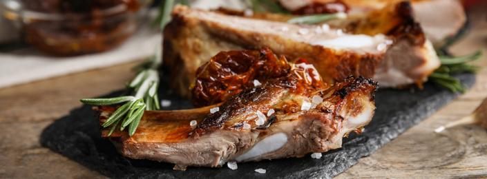 Tasty grilled ribs with rosemary on wooden table, closeup. Banner design