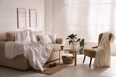 Photo of Comfortable sofa with blanket in stylish room