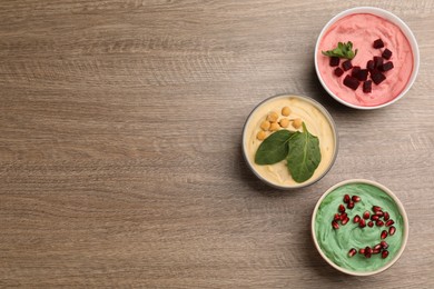 Photo of Different kinds of tasty hummus on wooden table, flat lay. Space for text