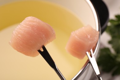 Photo of Fondue pot and forks with pieces of raw meat on table, closeup