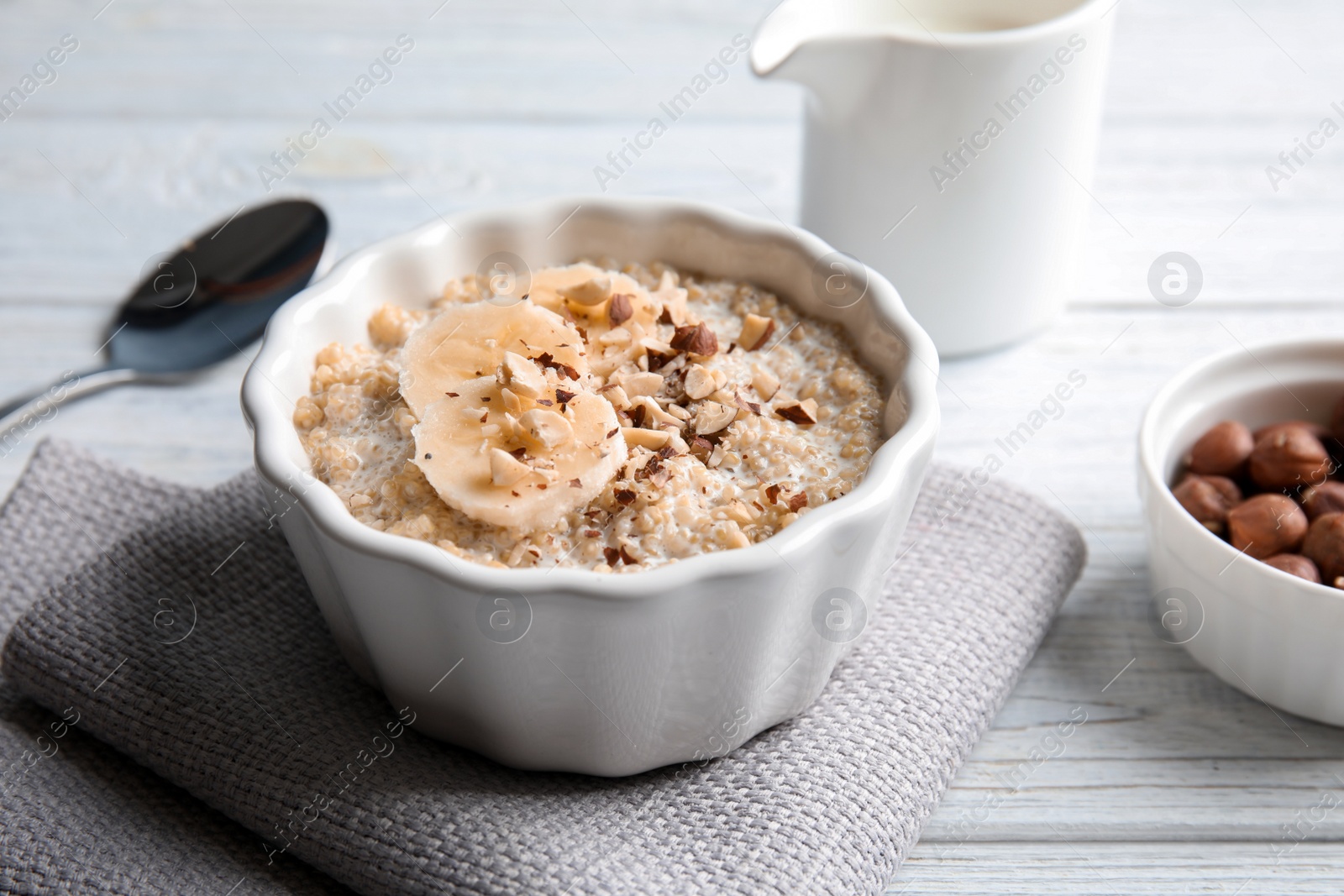 Photo of Quinoa porridge with banana and nuts in bowl served for breakfast on white wooden table
