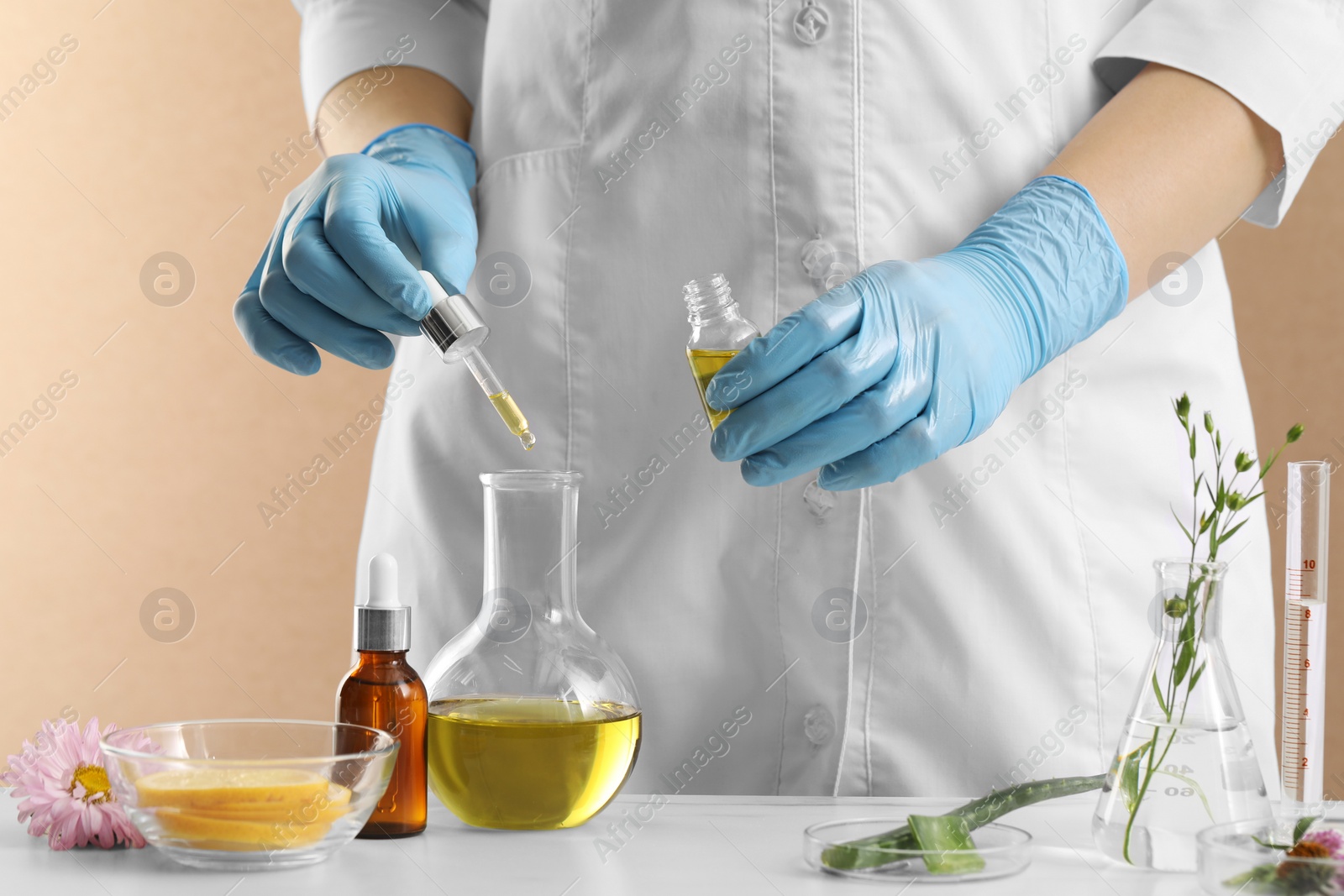 Photo of Scientist developing cosmetic oil at white table, closeup