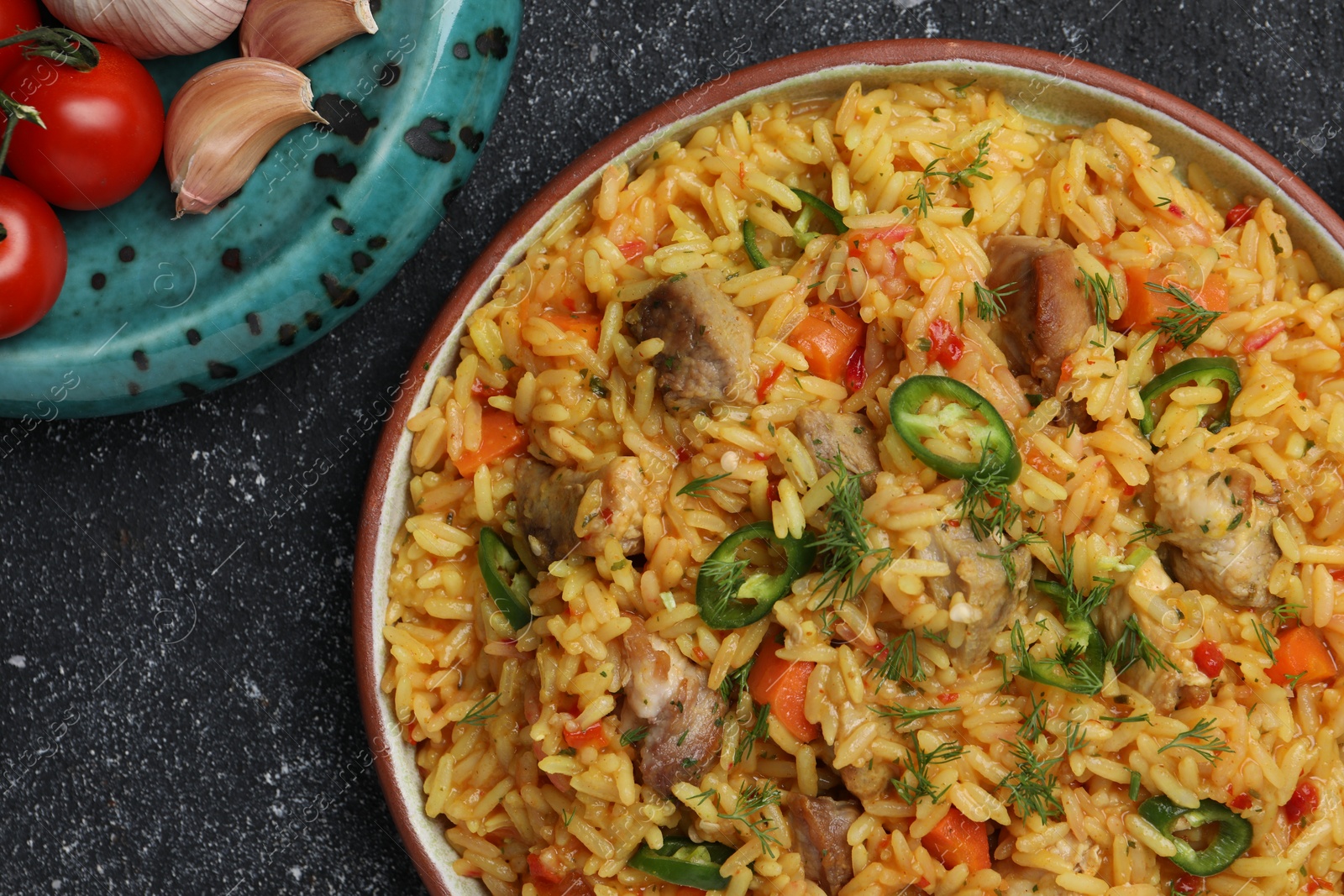 Photo of Delicious pilaf with meat and ingredients on black textured table, flat lay