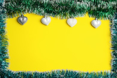 Frame of shiny bright tinsel and Christmas baubles on yellow background, flat lay. Space for text