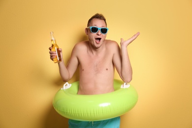 Photo of Shirtless man with inflatable ring and bottle of drink on color background