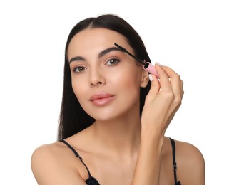 Beautiful young woman applying mascara on white background