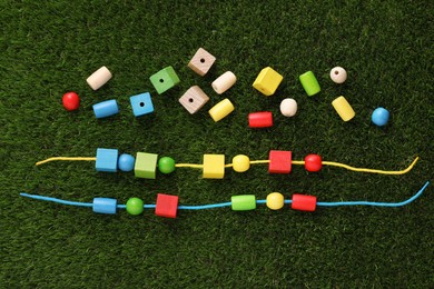 Photo of Wooden pieces and strings for threading activity on artificial grass, flat lay. Educational toy for motor skills development