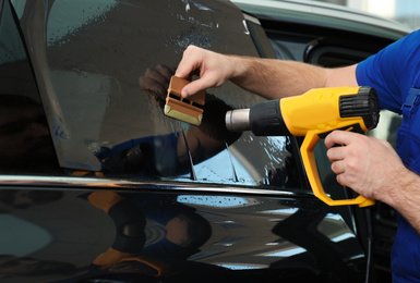 Photo of Worker tinting car window with heat gun in workshop, closeup