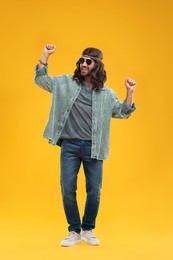 Photo of Stylish hippie man in sunglasses dancing on orange background