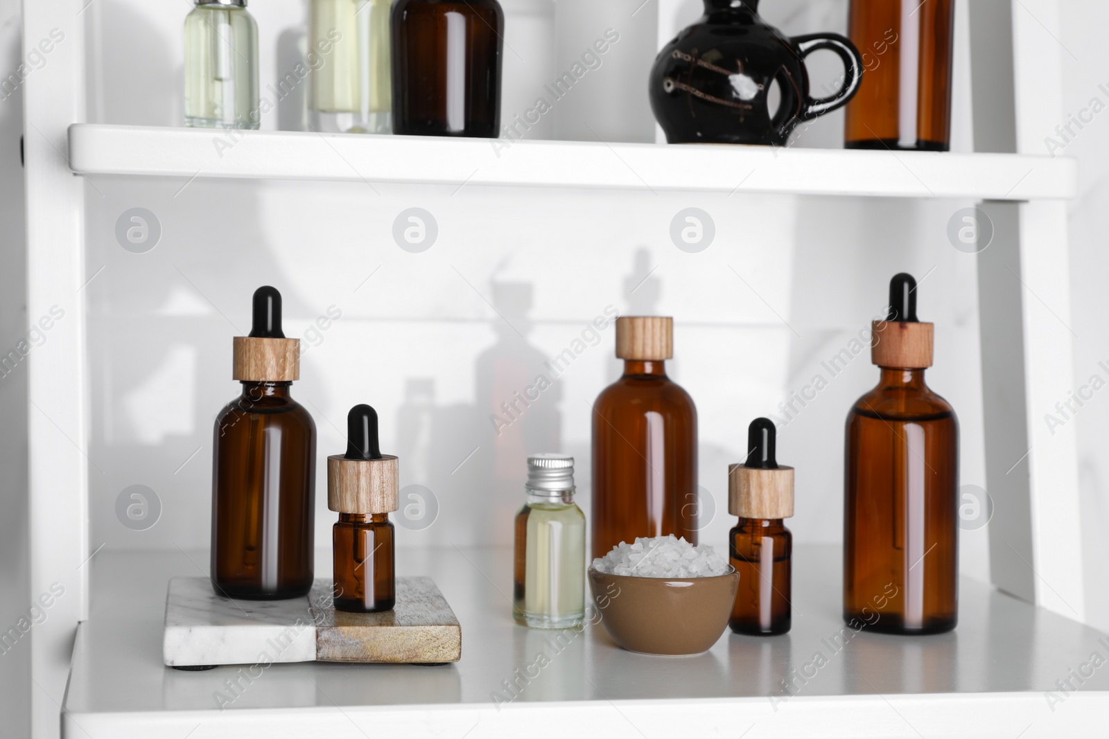 Photo of Essential oils, sea salt, and other cosmetic products on white shelving unit in bathroom